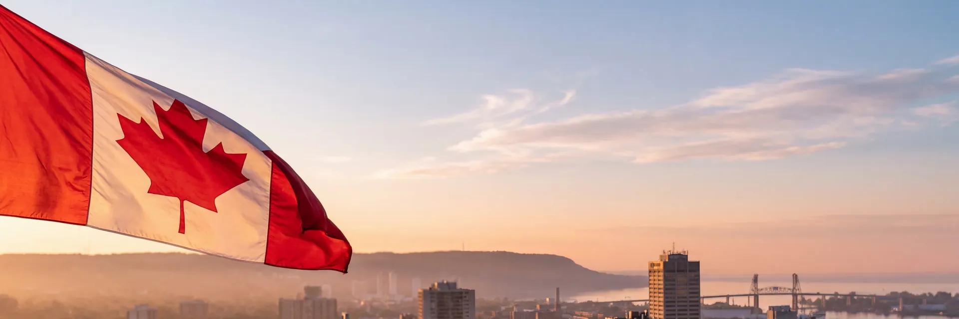 A Canadian flag waving in the foreground at dawn, with the Hamilton, Ontario skyline and Hamilton Harbour in the background.